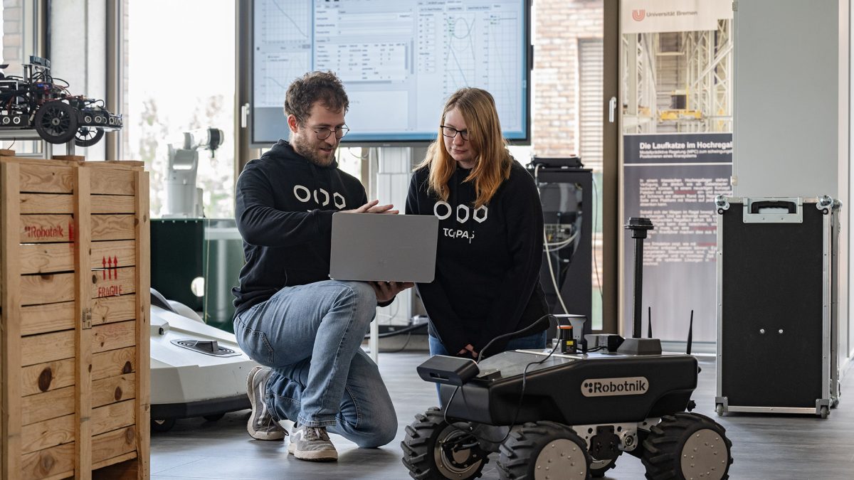 Eine Frau und ein Mann programmieren an einem Laptop einen Roboter